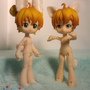 May include: Two nude-colored articulated dolls with yellow hair and white bunny ears. The dolls are posed in different positions on a light blue fuzzy surface.