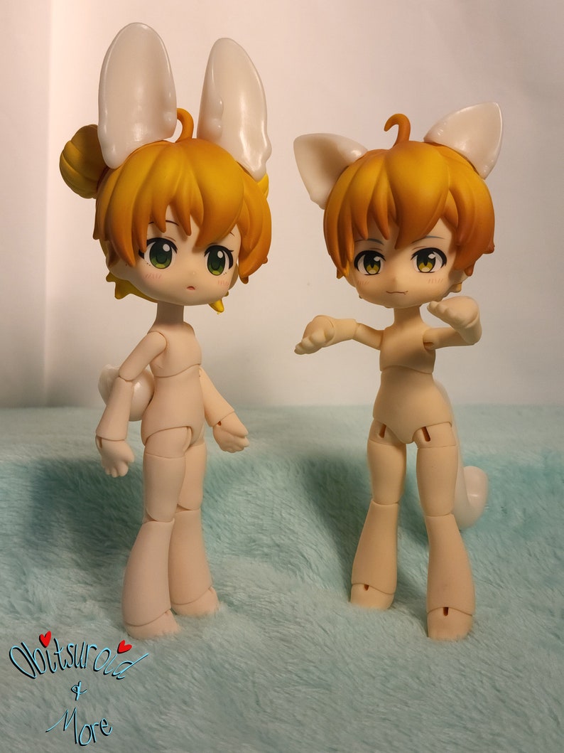 May include: Two nude-colored articulated dolls with yellow hair and white bunny ears. The dolls are posed in different positions on a light blue fuzzy surface.