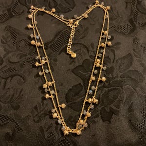 以下が含まれることがあります： 2連のゴールドトーンネックレス。小さな丸いビーズと、小さなイリデッセントビーズのクラスターで飾られています。ネックレスは調節可能なチェーンと繊細でフェミニンなデザインで、様々な場面に適しています。