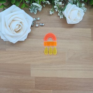 May include: A set of acrylic earrings in orange and yellow. The earrings are shaped like a half circle with three teardrop shapes hanging from the bottom.