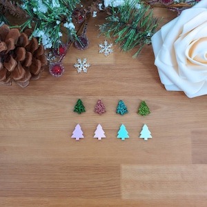 May include: Assortment of small, glittery Christmas tree ornaments in various colors, including green, pink, and blue. The ornaments are arranged in two rows on a wooden surface.