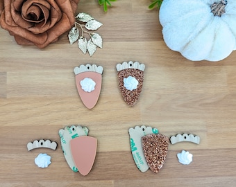 May include: Wooden acorn-shaped craft pieces with a cream-colored swirl design. One acorn is a solid peach color, and the other is covered in copper glitter. Additional pieces include small wooden crowns and cream-colored swirls.