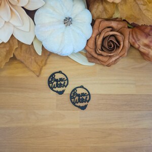 May include: Two black wooden earrings with the words "Basic Witch" written in a cursive font.
