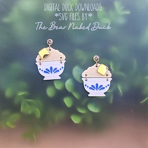 May include: A pair of dangle earrings shaped like white bowls with blue floral patterns, filled with beige textured material and topped with a small gold square. The text DIGITAL DUCK DOWNLOADS *SVG FILES BY* The Bear Naked Duck is visible.