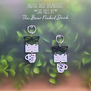 May include: A pair of dangle earrings featuring silver-toned hoops attached to black glasses, an open book with black text lines, and a white mug with a blue and pink floral pattern. The text DIGITAL DUCK DOWNLOADS *SVG FILES BY* The Bear Naked Duck appears above.