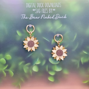 May include: A pair of hoop earrings featuring sunflower charms with cream-colored petals, a dark brown center, and gold glitter accents. The text above reads: DIGITAL DUCK DOWNLOADS *SVG FILES BY* The Bear Naked Duck.