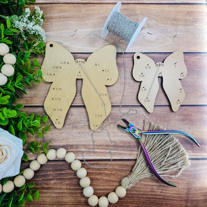 May include: A craft supplies arrangement on a wooden surface. Includes three wooden butterfly-shaped templates with measurements, a spool of silver chain, a pair of rainbow-colored pliers, and a beaded garland. The word "glare" is visible on one template.