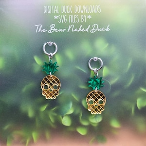 May include: A pair of silver-toned hoop earrings featuring dangling charms shaped like skulls with a gold-colored grid pattern and green acrylic leaves on top. The text DIGITAL DUCK DOWNLOADS *SVG FILES BY* The Bear Naked Duck is visible above.