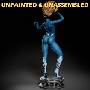 May include: Unpainted and unassembled blue figurine of a woman with blonde hair, wearing a silver and blue suit, standing on a black base.