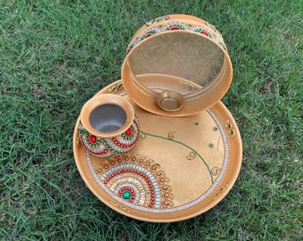 May include: A gold-colored metal tray with a round mirror, a small pot, and decorative embellishments. The tray is decorated with green and red jewels and a gold design.