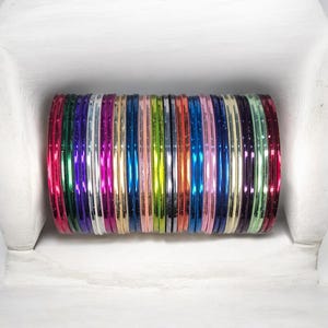 May include: A collection of colorful bangles in various shades, including pink, green, blue, and silver. The bangles are stacked together, creating a vibrant display of accessories. The image is taken from a close-up angle, highlighting the details of each bangle.