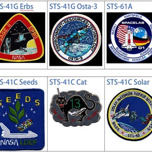 May include: A collection of nine NASA space shuttle mission patches. The patches are circular, triangular, and oval shaped and feature a variety of designs, including the American flag, a satellite, a cat, and a plant. The patches are all embroidered and have a blue, white, and red colour scheme.