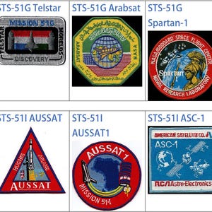 May include: A collection of nine space mission patches, each with a unique design and color scheme. The patches feature various spacecraft, astronauts, and mission names, such as "STS-51G Telstar", "STS-51G Arabsat", and "Soyuz TM-7".