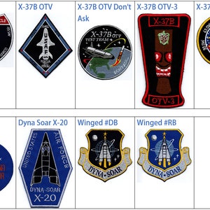 Puede incluir: Una colección de nueve parches bordados con varios diseños de temática espacial. Los parches son circulares, cuadrados y en forma de diamante y presentan una variedad de colores, incluyendo rojo, azul, blanco, negro y amarillo. Los parches incluyen texto como "X-37B OTV", "Dyna Soar" y "OTV-3".