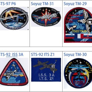 May include: A collage of nine embroidered patches, each representing a different space mission. The patches feature a variety of designs, including space shuttles, rockets, and astronauts. The patches are all circular or oval in shape and have a white background with colorful embroidery.