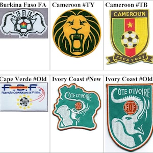 May include: A selection of embroidered football association patches. Designs include a lion, a scorpion, and soccer balls, with text such as "Angola FA", "Cameroon", and "Ivory Coast". The patches are in various colours, including green, red, and gold.