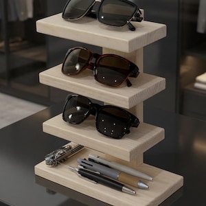 May include: A wooden display stand with four tiers, showcasing sunglasses and accessories. The top tier holds black sunglasses with a gold frame. The second tier features brown tortoiseshell sunglasses. The third tier displays black sunglasses. The bottom tier has a pocket knife and pens.