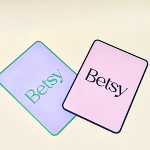May include: Two rectangular cards, one lavender with a green border and the word "Betsy" in green, and the other pink with a black border and the word "Betsy" in black.