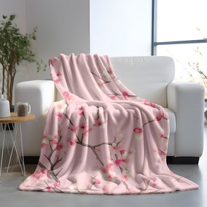 May include: A soft pink fleece throw blanket with a delicate floral pattern of pink and white cherry blossoms on branches.