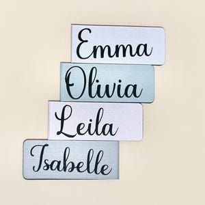 May include: Four personalised name tags with the names Emma, Olivia, Leila, and Isabelle. The tags are made of a light grey material with a subtle texture and black lettering.