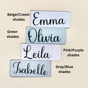 May include: Four personalised name plaques in different colours. The names are Emma, Olivia, Leila, and Isabelle. The plaques are in beige, green, pink, and grey shades.