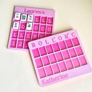May include: Two pink Mahjong game boards with the names "Lauren's" and "Katherine" printed on them. One board has Mahjong tiles in place. The boards have a grid of rectangular slots for the tiles.