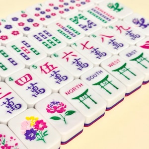 May include: A collection of white Mahjong tiles with various symbols and numbers in red, green, purple, and black. Some tiles feature floral designs. The tiles are arranged in a diagonal pattern.