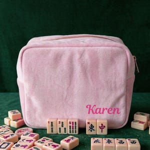 Op de afbeelding: Een roze fluwelen cosmetische tas met de naam "Karen" op de voorkant. De tas is rechthoekig met een ritssluiting. Mahjong-tegels zijn voor de tas gerangschikt.