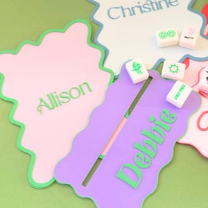 May include: Three personalized name tags with scalloped edges and green trim. The tags are pink, purple, and blue. The names "Allison", "Debbie", and "Christine" are written in green on the tags.