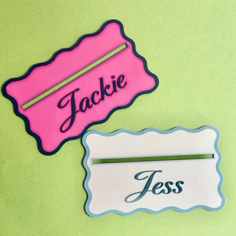 May include: Two personalized name cards with wavy edges. The top card is pink with a navy blue border and the name "Jackie" written in navy blue cursive. The bottom card is white with a light blue border and the name "Jess" written in light blue cursive.