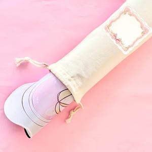 May include: A cream drawstring bag with a decorative label on a pink background. Inside the bag is a rolled-up yoga mat with a pink and white floral design. The mat is partially visible.