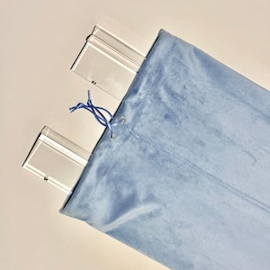 May include: A light blue fabric bag with a drawstring closure, holding several clear, rectangular items. The bag has metal grommets and a blue drawstring. The items inside appear to be clear, possibly acrylic or glass.