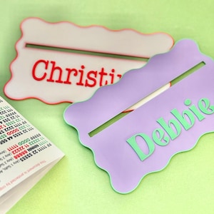 May include: Two personalized name tags with wavy edges. The top tag is white with red lettering that says "Christy". The bottom tag is purple with green lettering that says "Debbie".