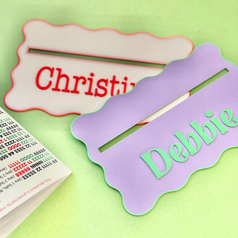 May include: Two personalized name tags with wavy edges. The top tag is white with red lettering that says "Christy". The bottom tag is purple with green lettering that says "Debbie".