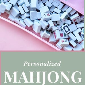May include: A pink zipped pouch filled with white Mahjong tiles. The pouch is personalised with the name "Emily" in teal script. The image also shows a pouch with the name "Stacey" and the text "Personalised Mahjong Gift Ideas".