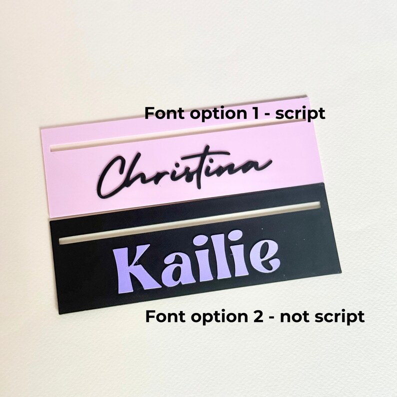 May include: Two nameplates with different font styles. The top nameplate is pink with black script font that says "Christina". The bottom nameplate is black with a purple font that says "Kailie".