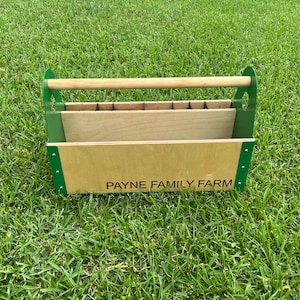 Pode incluir: Uma caixa de ferramentas de madeira com uma moldura de metal verde e uma al&ccedil;a de madeira. A caixa tem um r&oacute;tulo que diz "PAYNE FAMILY FARM".