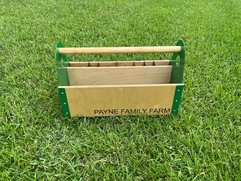Pode incluir: Uma caixa de ferramentas de madeira com uma moldura de metal verde e uma al&ccedil;a de madeira. A caixa tem um r&oacute;tulo que diz "PAYNE FAMILY FARM".