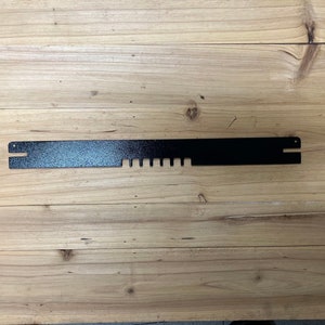 May include: A black metal bar with a series of evenly spaced holes along its length. The bar is approximately 12 inches long.