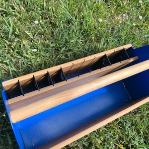 Pode incluir: Um caddy de ferramentas de metal azul com uma al&ccedil;a de madeira e divis&oacute;rias. O caddy tem uma base de madeira e &eacute; projetado para guardar ferramentas ou outros itens pequenos.