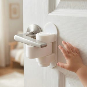 May include: A white plastic door handle lock installed on a white door. The lock is designed to prevent children from opening the door. A child's hand is reaching for the door.