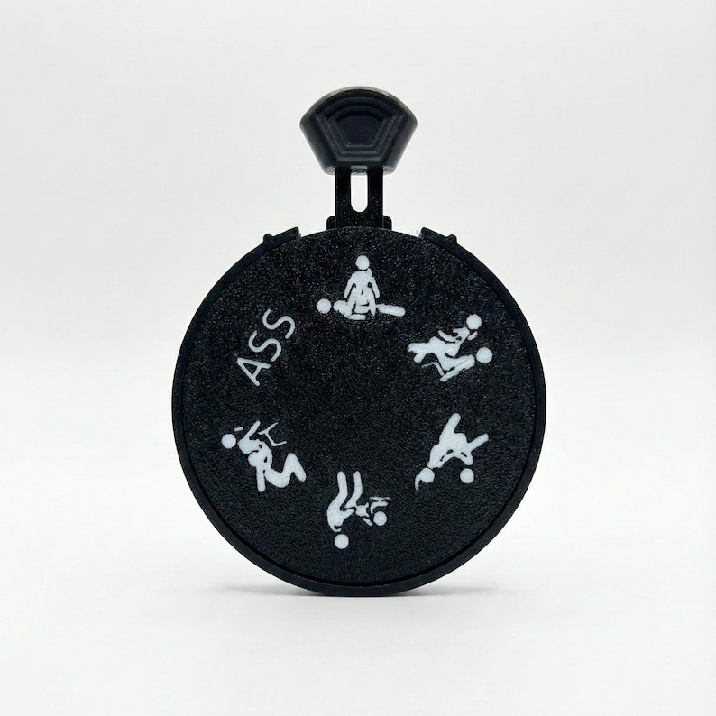 May include: A black, circular novelty item with a handle. The word "ASS" is printed on the item. White stick figures illustrate various sexual positions around the circle.