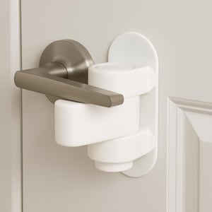 May include: A white door lever lock installed on a door. The lock is made of white plastic and is designed to prevent children from opening the door. The door handle is silver.