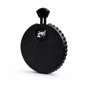 May include: A black, circular flask with a textured surface and a ridged edge. It features a small, white graphic and a black handle on top. The flask is designed for carrying liquids.