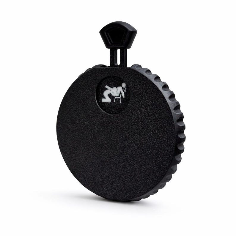 May include: A black, circular flask with a textured surface and a ridged edge. It features a small, white graphic and a black handle on top. The flask is designed for carrying liquids.