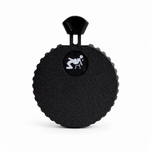 May include: A black, circular product with a textured surface and a small, white graphic of a person sitting in a chair. The product has a hexagonal handle at the top. The overall design is simple and modern.