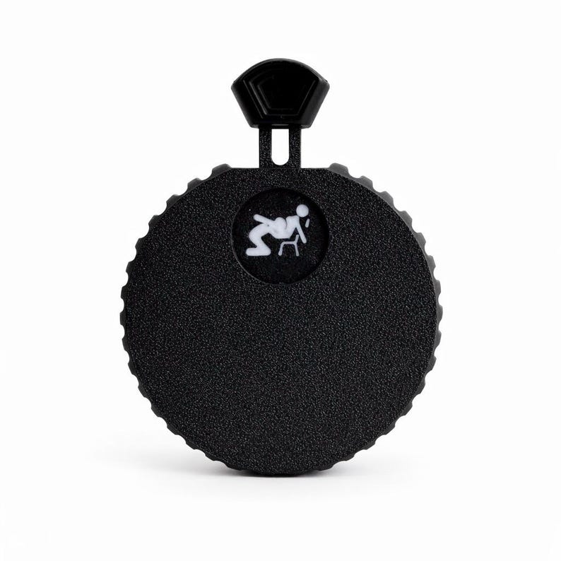 May include: A black, circular product with a textured surface and a small, white graphic of a person sitting in a chair. The product has a hexagonal handle at the top. The overall design is simple and modern.