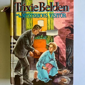 May include: A vintage book cover featuring a colorful illustration of a man and a girl in a room. The book title is "Trixie Belden and the Mysterious Visitor".
