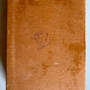 K&ouml;nnte beinhalten: Ein brauner Karton mit einem abgenutzten und verblassten Aussehen. Der Karton hat einen kleinen, verblassten lilafarbenen Stempel auf der Vorderseite.
