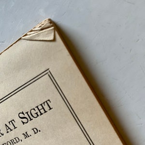 K&ouml;nnte beinhalten: Nahaufnahme des Einbands eines Buches mit dem Titel "At Sight" von K. Ford, M.D. Unter dem Titel steht der Text "Comb, Editor".